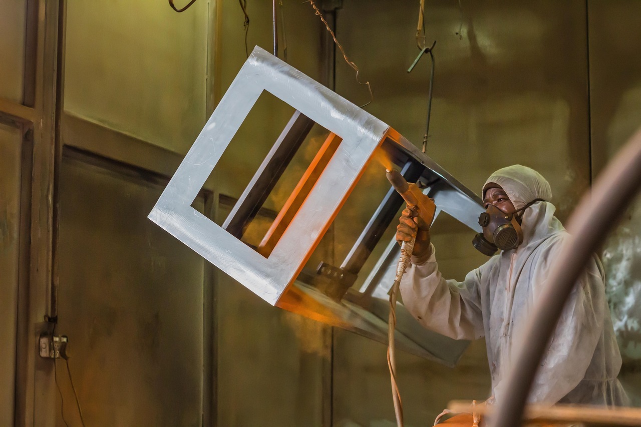 Technician powder coating a metal part with a spray gun